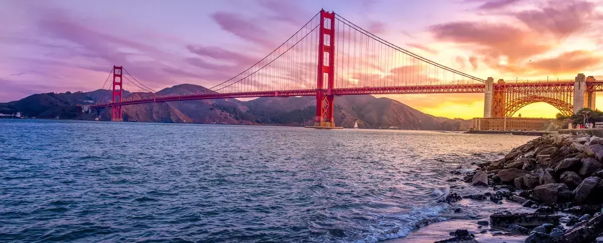 Die Golden Gate Bridge bei Sonnenuntergang mit einem bunten Himmel und der San Francisco Bay im Vordergrund.